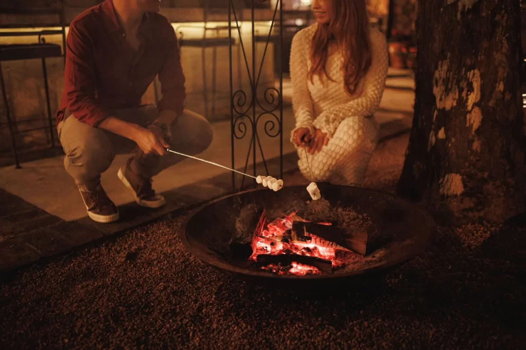 Casal assando marshmallows em uma fogueira ao ar livre durante a noite em Gramado, criando um ambiente aconchegante e romântico na Serra Gaúcha.