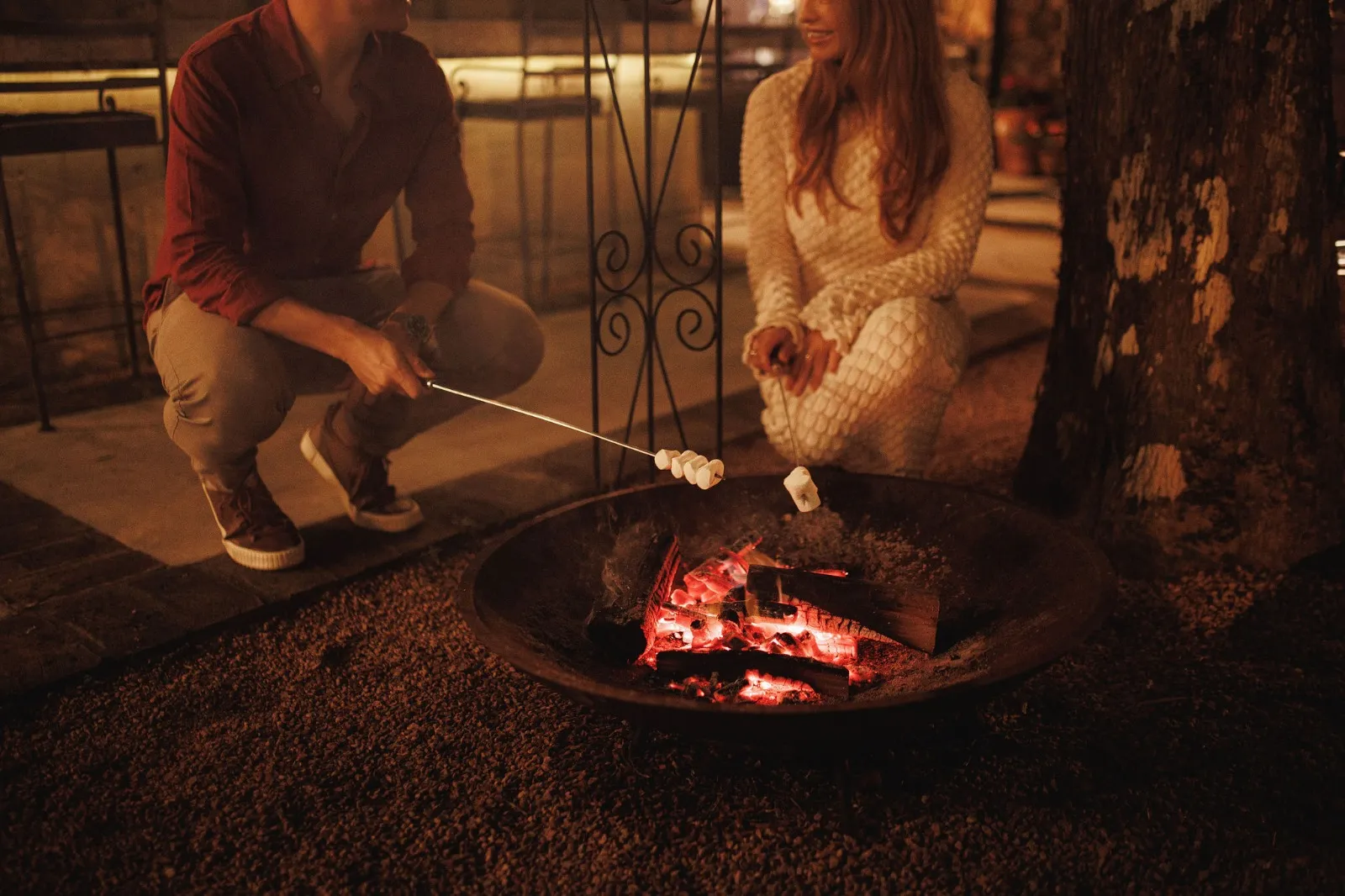 Casal assando marshmallows em uma fogueira ao ar livre durante a noite em Gramado, criando um ambiente aconchegante e romântico na Serra Gaúcha.